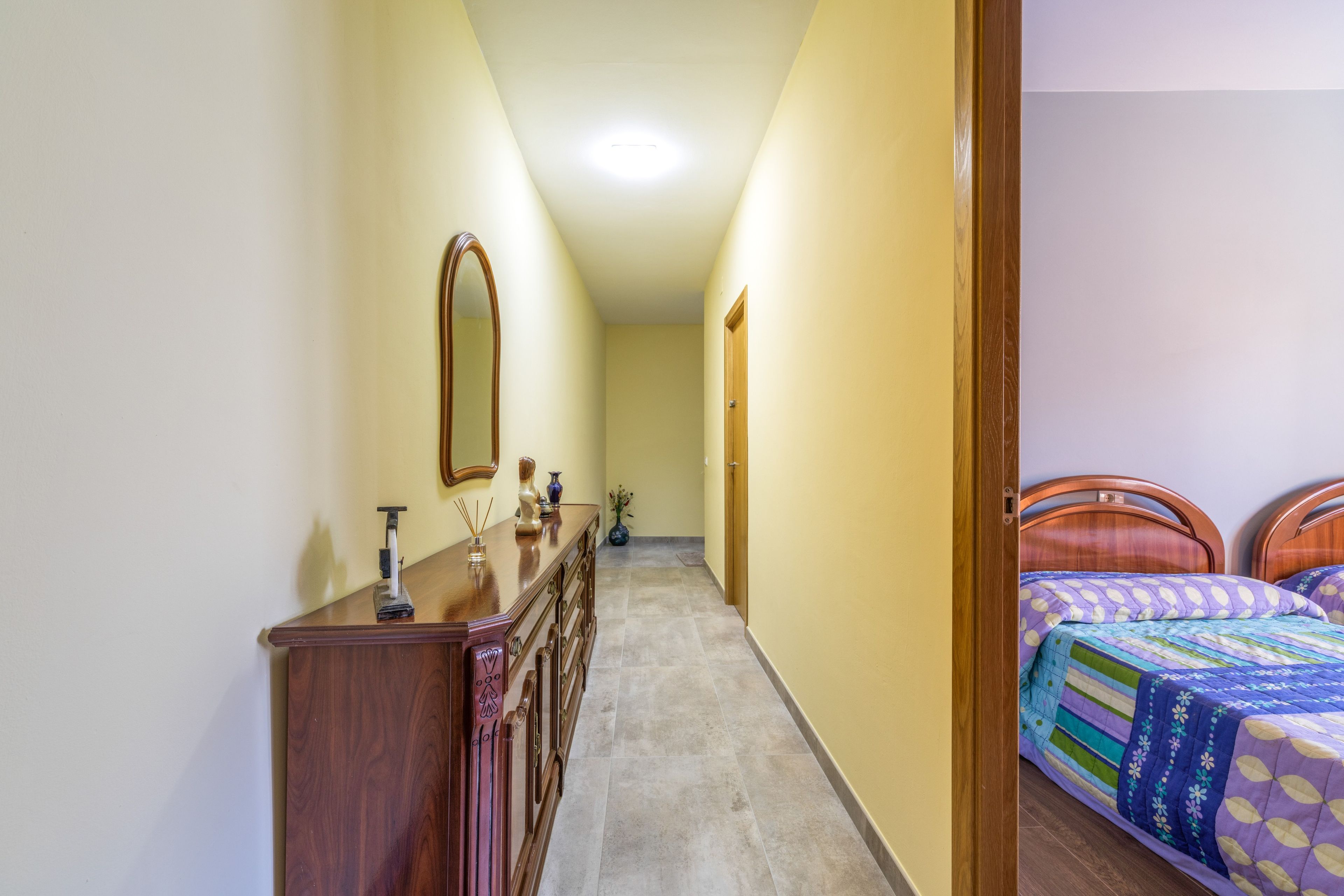 Un corridoio stretto con una cassettiera in legno, uno specchio e una porta che dà su una camera da letto con due letti.