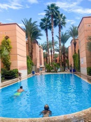 A swimming pool surrounded by palm trees and buildings. - Riad zineb  (Marrakech)