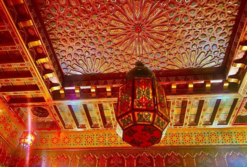 Un soffitto con elaborate decorazioni geometriche e un lampadario pendente.