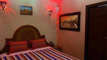 Un dormitorio con cama, cabecera, dos lámparas de pared y dos cuadros enmarcados.