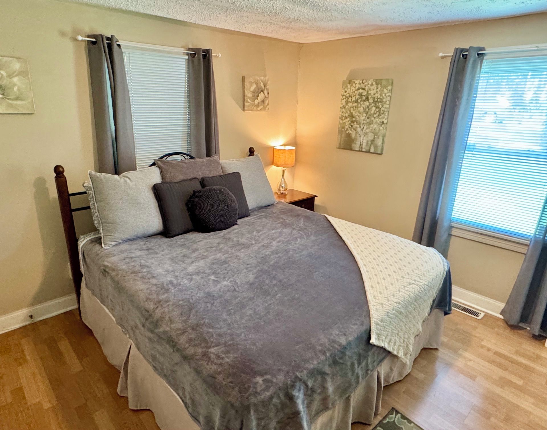 A bedroom with a bed, curtains, a nightstand, a lamp, and a wall art piece.