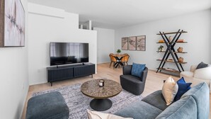 A modern living room with a flat-screen TV, comfortable seating, a coffee table, and a bookshelf. - Stylish 850 SF SoHo 1BR W/D (New York)