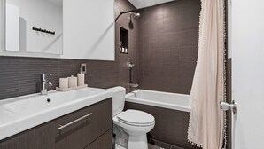 A modern bathroom with a bathtub, toilet, and vanity. - Stylish 850 SF SoHo 1BR W/D (New York)