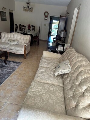 A living room with two sofas, a dining table, and a kitchen area in the background. - Cozy 2-bedroom house in quaint Ocho Rios with AC (Ocho Rios)
