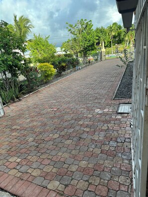A paved walkway with a metal fence and greenery on one side, leading to a gated entrance. - Cozy 2-bedroom house in quaint Ocho Rios with AC (Ocho Rios)