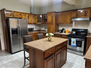 A kitchen with wooden cabinets, stainless steel appliances, a granite countertop, and a small island with a vase. - Cozy 2-bedroom house in quaint Ocho Rios with AC (Ocho Rios)