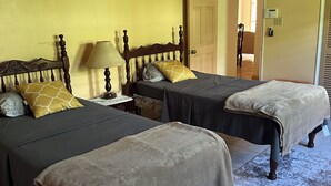 Ein Zimmer mit zwei Betten, einem Nachttisch, einer Lampe und einer Tür zu einem anderen Raum.