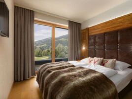 A bedroom with a large bed, a wooden headboard, and a view of a mountainous landscape.