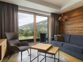 A modern living room with a sofa, a chair, a wooden coffee table, and a view of a mountainous landscape through large windows.