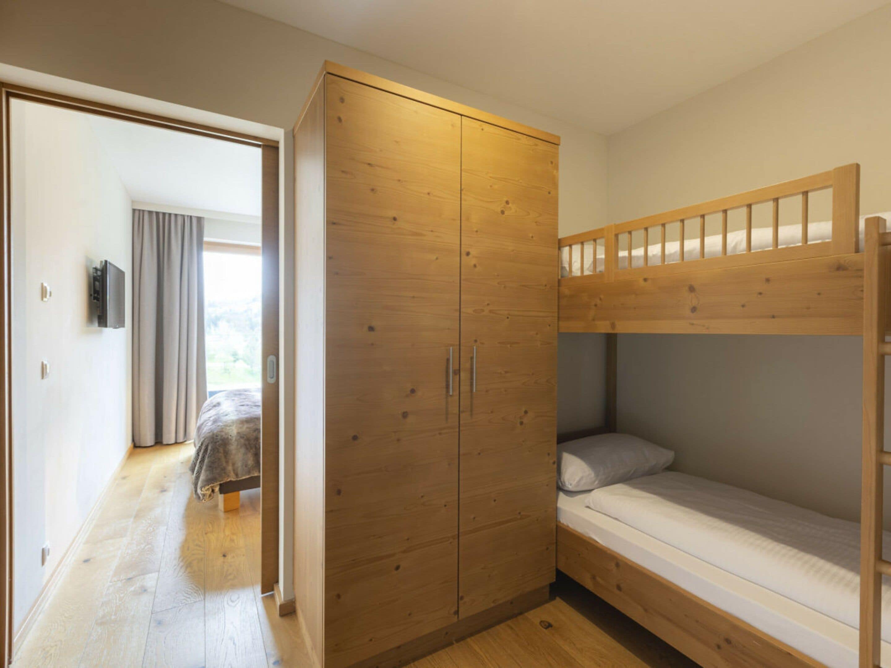A room with a bunk bed, a wooden wardrobe, and a door leading to another room.