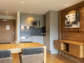 A modern kitchen with built-in appliances, a dining area with a wooden table and chairs, and a rustic wall with a framed picture. - Family Apartment for up to 6 People (Westendorf)