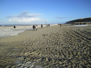 Une plage de sable avec des empreintes et une structure en bois visible au loin.