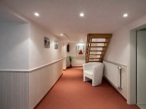 A narrow hallway with a white radiator, a white chair, and a wooden staircase. - Holiday Apartment With 3 Bedrooms (Norderney)