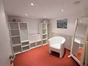 A room with a white chair, a large mirror, and a wardrobe with multiple shelves and drawers. - Holiday Apartment With 3 Bedrooms (Norderney)