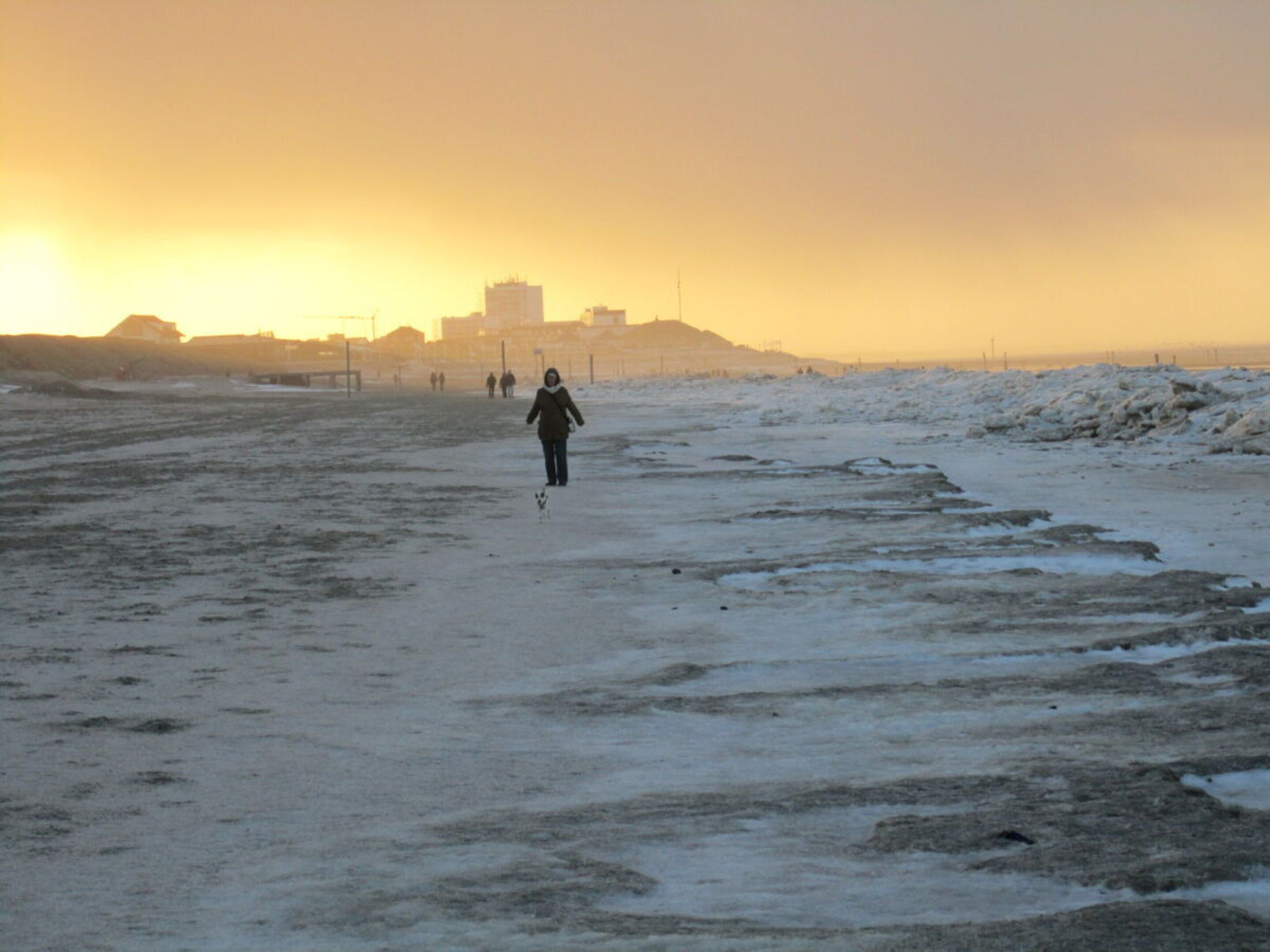 A person walking on a snow-covered path with buildings in the background.