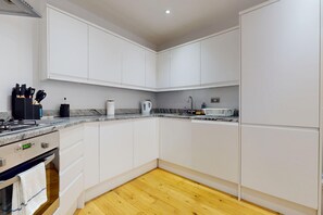 A modern kitchen with white cabinets, a granite countertop, a wooden floor, and a built-in oven. - Bright 3BR Flat w/Private Garden-Near Station (London)