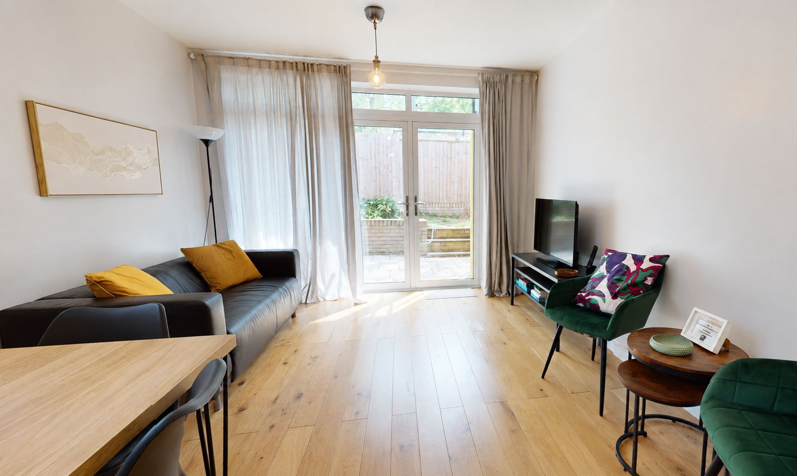 En moderne stue med sofa, fjernsyn, spisebord og en grøn lænestol.