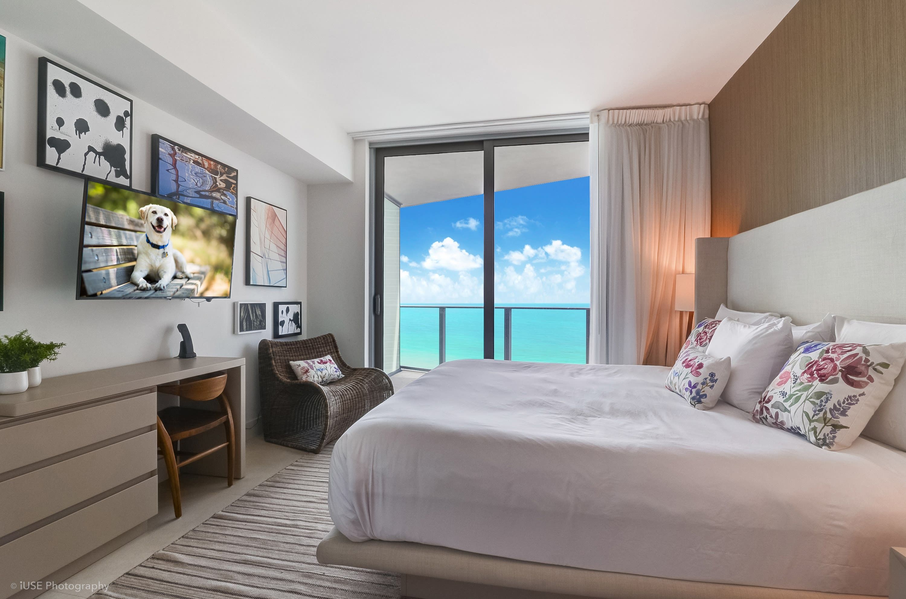A modern hotel room with a large bed, a desk, a chair, and a view of the ocean.