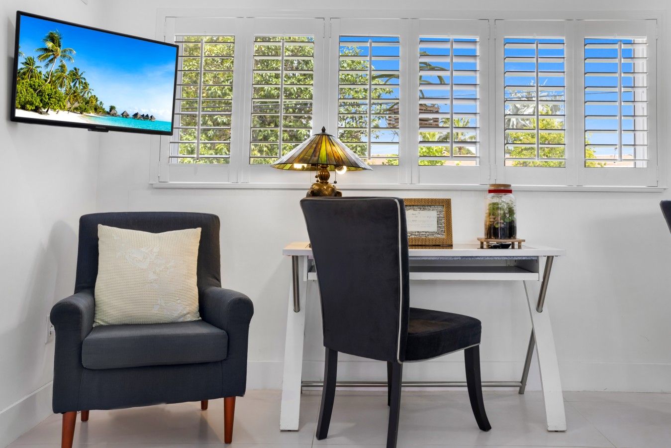 Una habitación con una televisión que muestra una playa tropical, un escritorio con una lámpara y dos sillas.