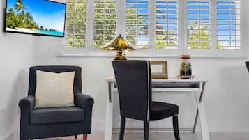 Una habitación con una televisión que muestra una playa tropical, un escritorio con una lámpara y dos sillas.