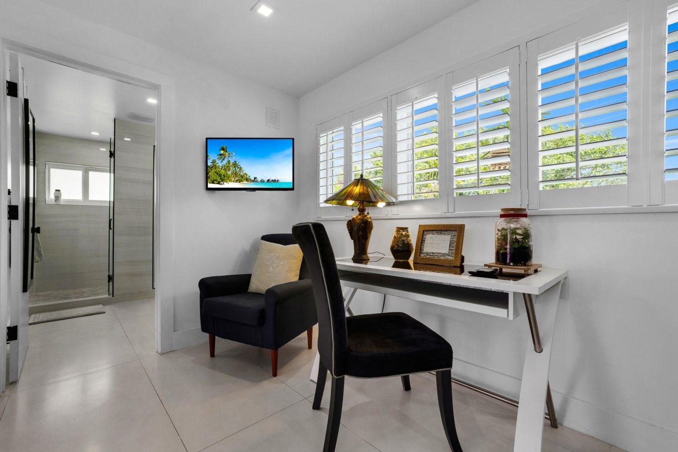 A modern room with a desk, chair, TV, and a view of greenery through the windows.