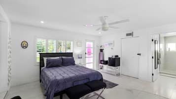 Un dormitorio moderno con cama, ventilador de techo, escritorio y baño con ducha.