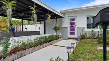 Een modern huis met een overdekte veranda, een betonnen pad en diverse planten en bloemen.