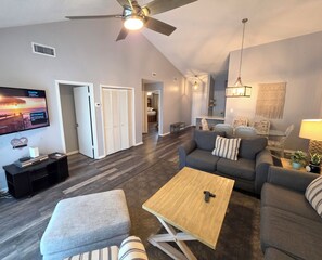 Een moderne woonkamer met een plafondventilator, een flatscreen televisie en een zithoek met een bank en fauteuils.