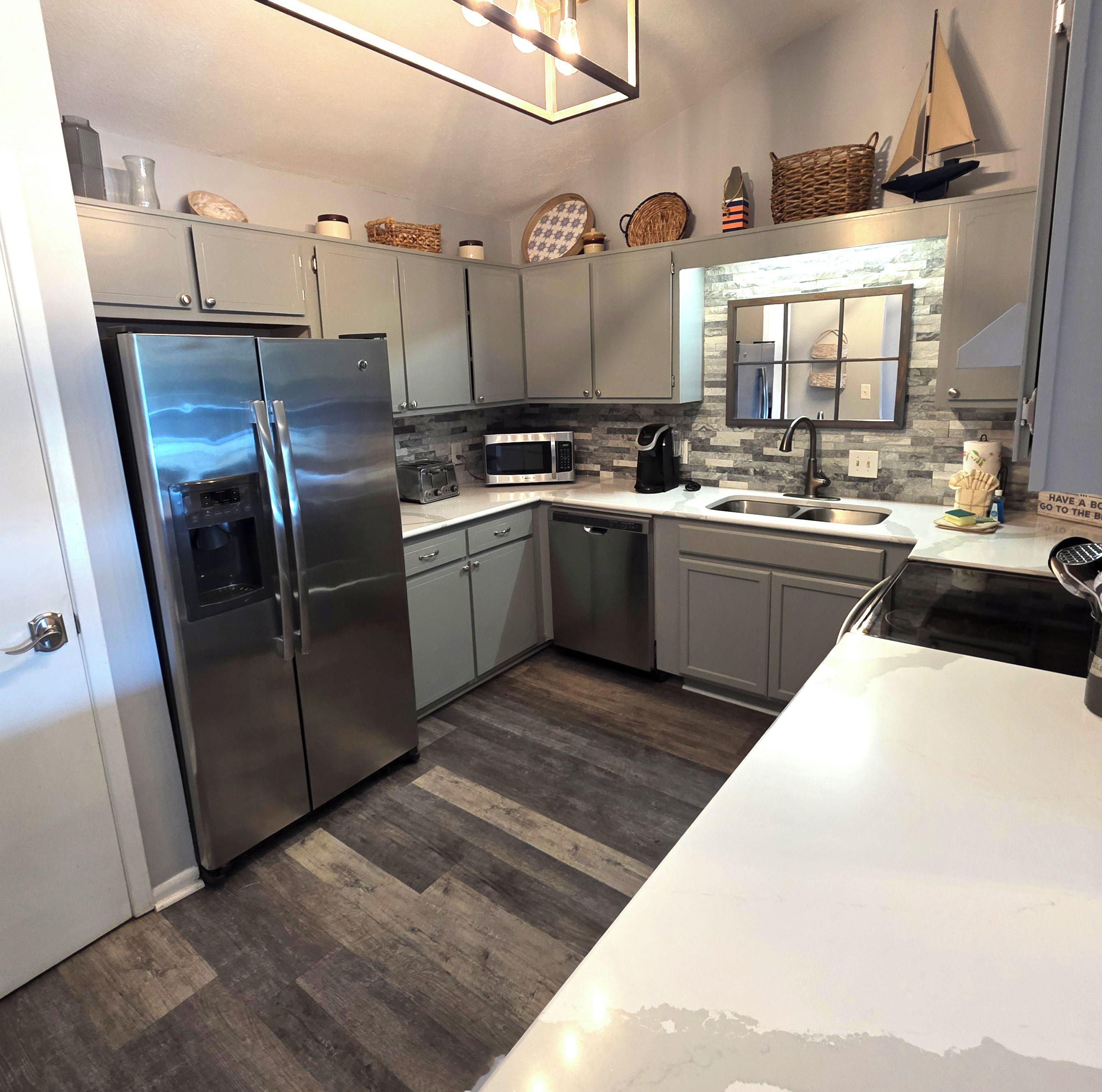 A modern kitchen with stainless steel appliances, grey cabinets, and a herringbone-patterned backsplash.