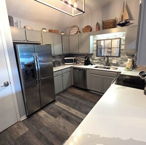 A modern kitchen with stainless steel appliances, grey cabinets, and a herringbone-patterned backsplash. - Chateau La Mer II #104 2-Bd 2-Bth 2nd Floor Close to Beach (Destin)