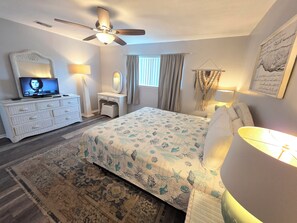Ein Schlafzimmer mit Bett, Kommode, Schminktisch, Deckenventilator und Fernseher.