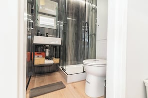 Un bagno moderno con cabina doccia in vetro, un water bianco e un pavimento in legno.