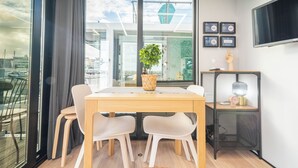 Um espaço de escritório moderno com uma mesa de madeira, cadeiras brancas, uma planta em vaso, luminária de mesa e uma televisão na parede.