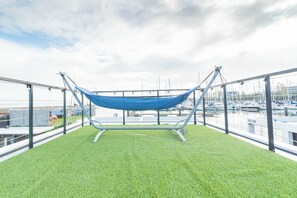 Un hamac installé sur un toit, avec du gazon synthétique, offrant une vue sur une marina remplie de bateaux.