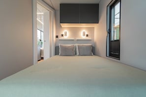 Una camera da letto con un letto, due comodini, una finestra con persiane e una porta che dà su un'altra stanza.