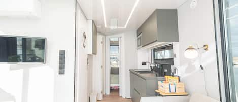 A compact living space with a kitchenette, a sofa, a television, and a window.