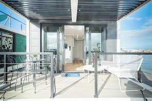 Zona relax esterna moderna con sedie e tavoli in metallo, ingresso con porta in vetro e vista sul mare.