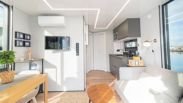 A modern kitchen with a built-in microwave, a dining area with a wooden table, and a sofa with a view of the water. - Vrbo Property (Lisboa)