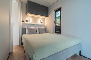 Une chambre à coucher avec un lit, une fenêtre avec des stores, une porte et des luminaires fixés au mur.