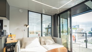 A modern living room with a sofa, a small wooden table, and a large window offering a view of the sea. - Vrbo Property (Lisboa)