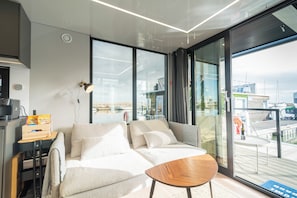 Ein modernes Wohnzimmer mit einer Couch, einem kleinen Holztisch und einem großen Fenster mit Meerblick.