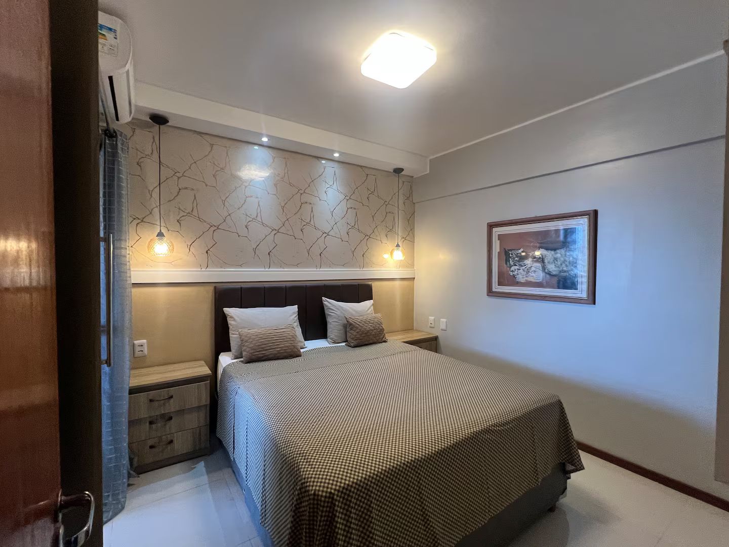 A bedroom with a bed, bedside tables, a wall-mounted light fixture, and a framed picture.
