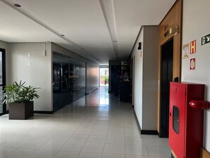 A hotel corridor with a glass elevator, a red fire safety cabinet, and a potted plant. - 1904 Nazaré · 2-bedroom apartment with garage in the neighborhood of (Belém)