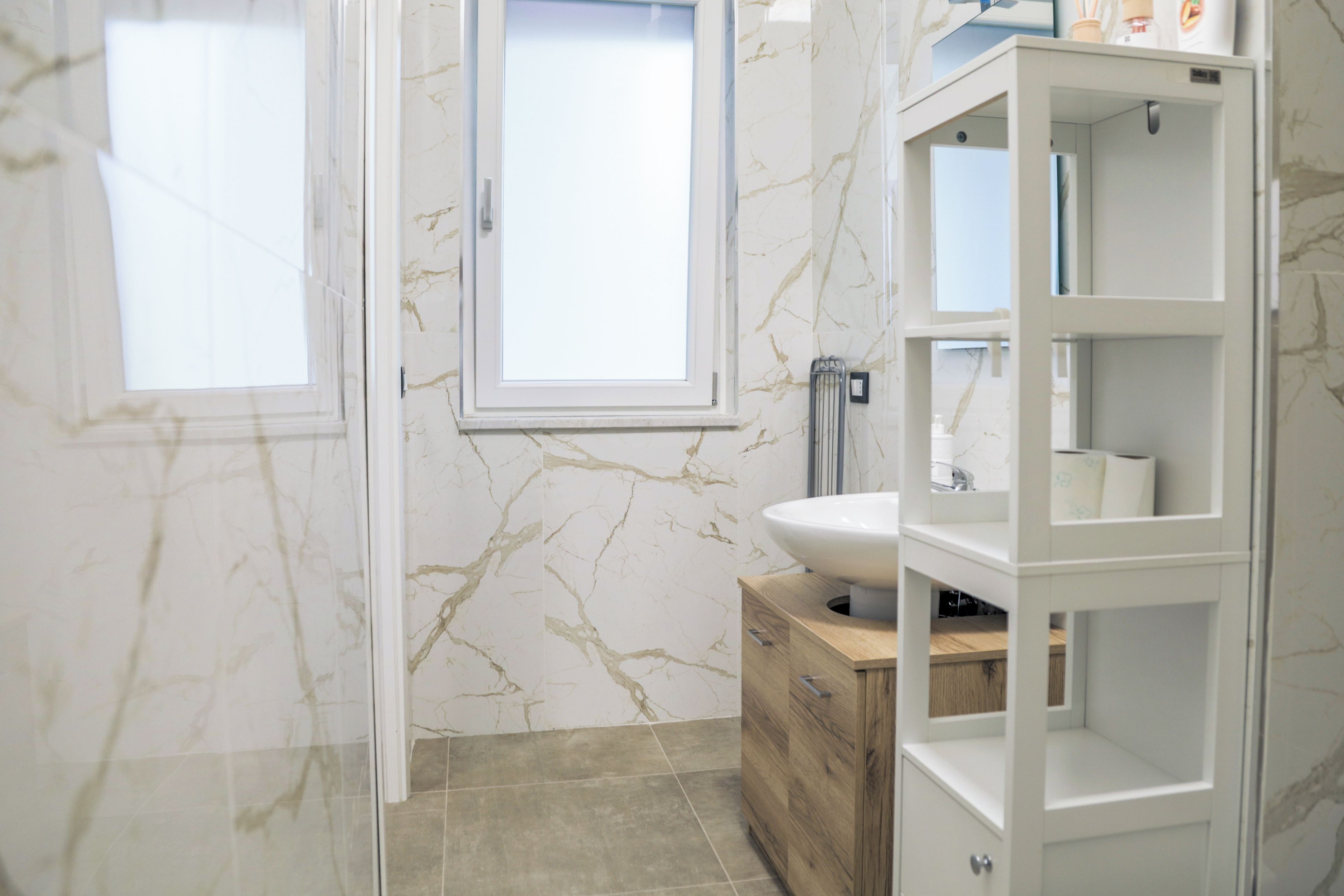 A modern bathroom with a marble wall, a window, a sink, and a wooden cabinet.