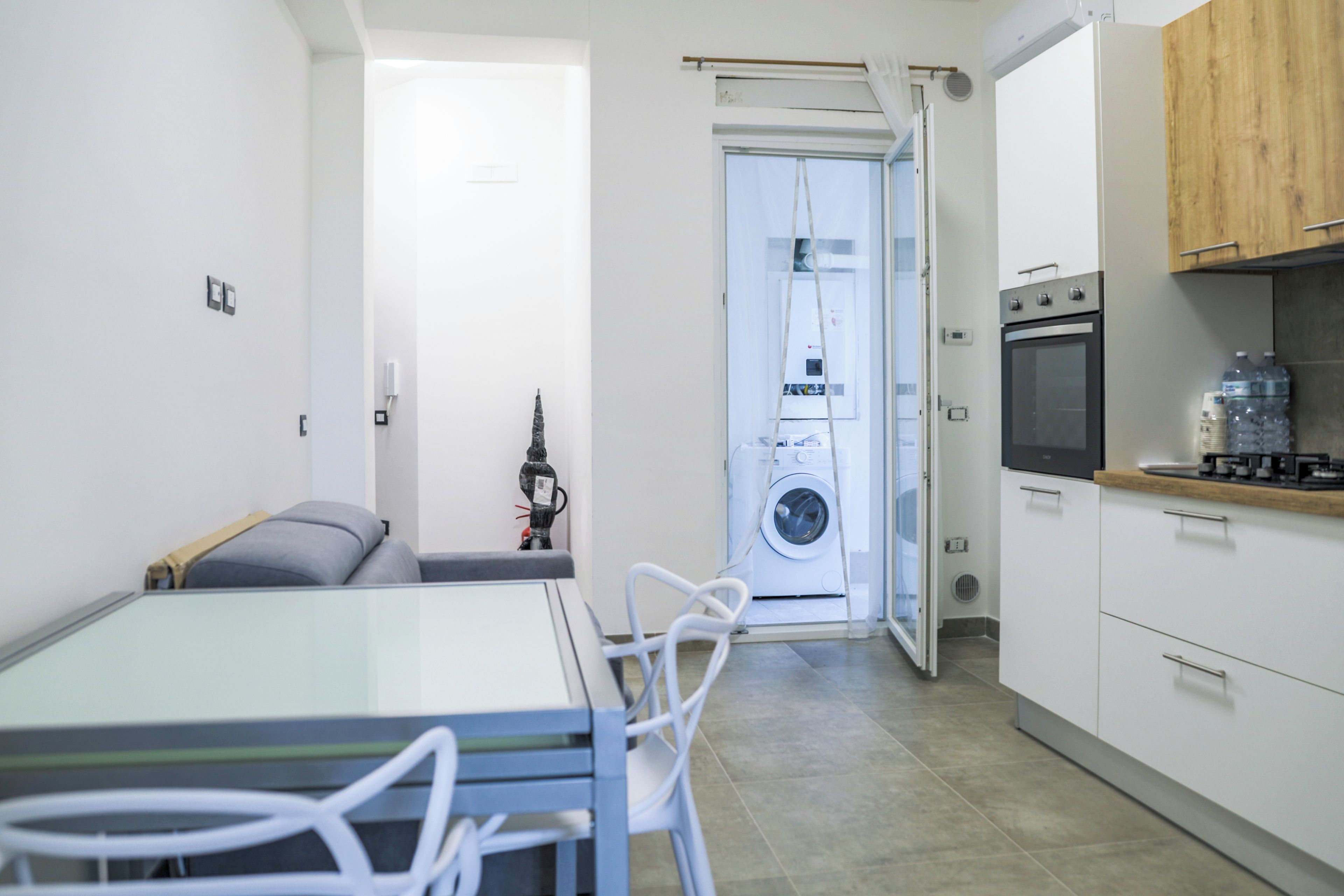 A compact kitchen with a built-in oven, a washing machine, and a dining area with a table and chairs.