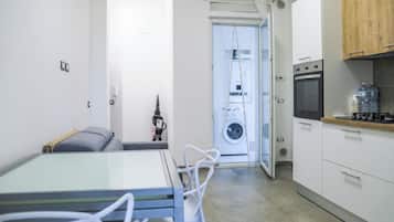 A compact kitchen with a built-in oven, a washing machine, and a dining area with a table and chairs.