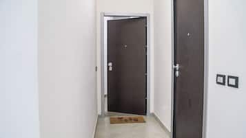 A narrow hallway with two doors, one closed and one open, leading to a room. There are two doormats on the floor.