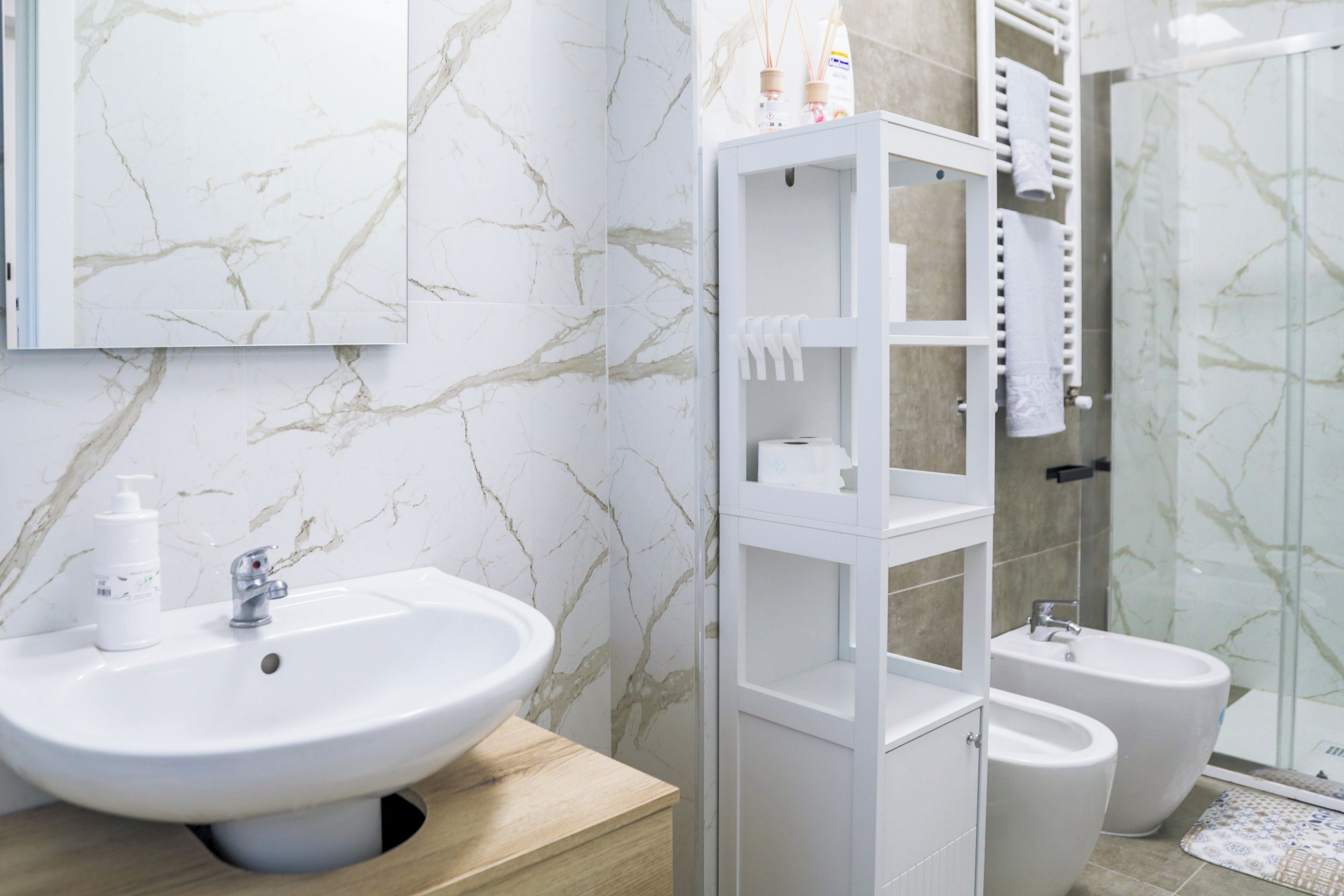 A bathroom with a marble wall, a white sink, a toilet, and a glass shower enclosure.