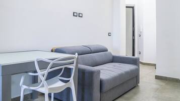 A modern living room with a grey sofa, a white chair, and a glass-top table.