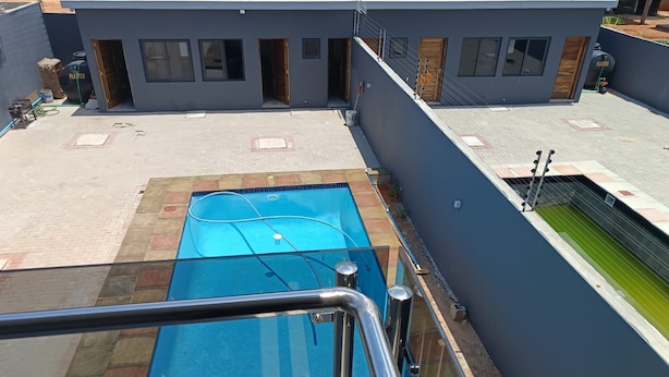 Piscina no terraço com barreira de vidro, piscina azul e edifício moderno com várias portas e janelas.